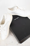 A pair of white leather Saint Laurent sneakers displayed next to their signature black box on a light marble surface.