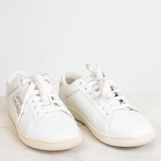 A pair of white leather low-top sneakers with white laces, displayed on a light marble surface against a white background.