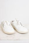 A pair of white leather low-top sneakers with white laces, displayed on a light marble surface against a white background.