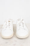 A pair of white leather low-top sneakers with white laces, resting on a light marble surface against a white background.