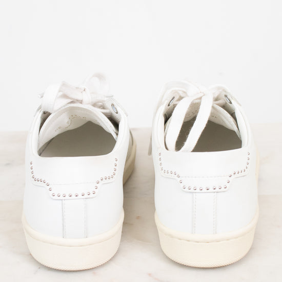 A pair of white leather low-top sneakers shown from the back, resting on a light marble surface against a white background.