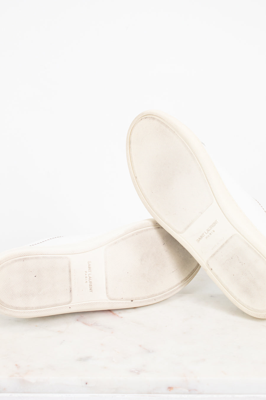 A pair of off-white leather shoes shown from the sole side, resting on a light marble surface against a white background.