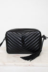 A black quilted leather shoulder bag with a prominent interlocking YSL logo on the front, resting on a light marble surface against a white background.