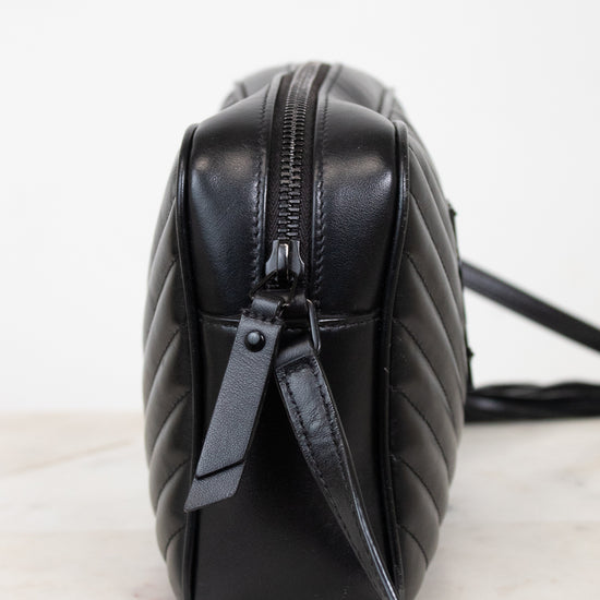 A black quilted leather shoulder bag shown from a side profile view, resting on a light marble surface against a white background.