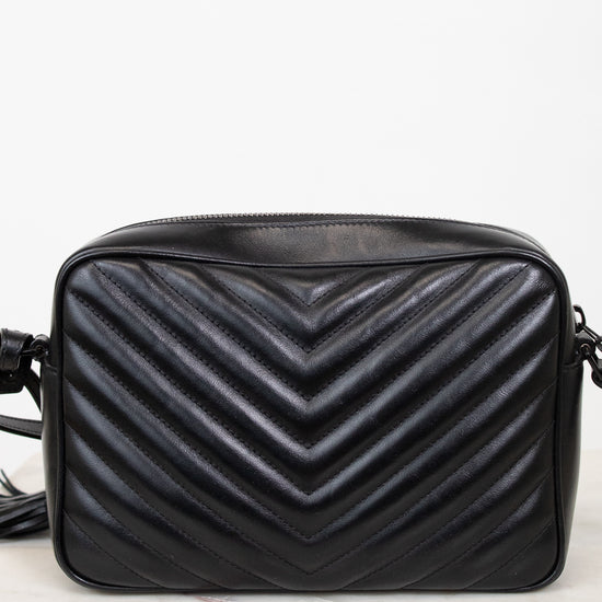 A black quilted leather crossbody bag with a prominent chevron pattern, resting on a light marble surface against a white background.