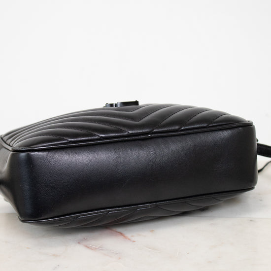 A black quilted leather handbag shown from a side angle, resting on a white marble surface against a white background.