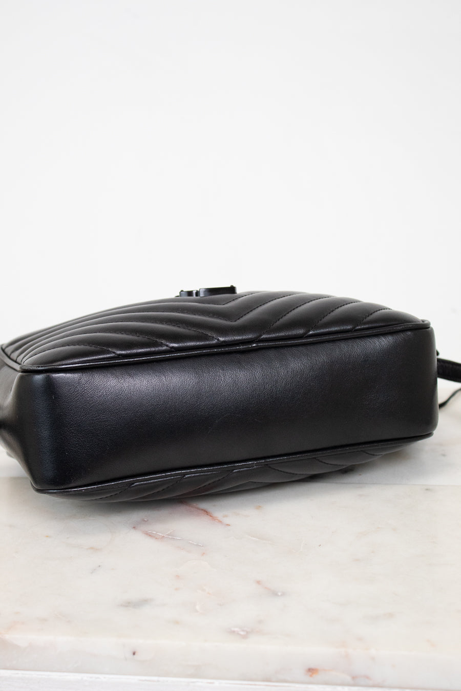 A black quilted leather handbag shown from a side angle, resting on a white marble surface against a white background.