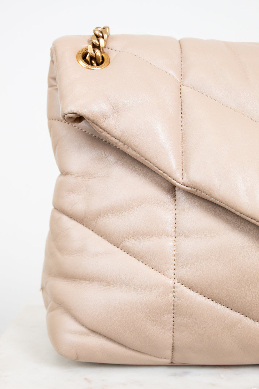 Beige quilted handbag with gold chain detail on a white background