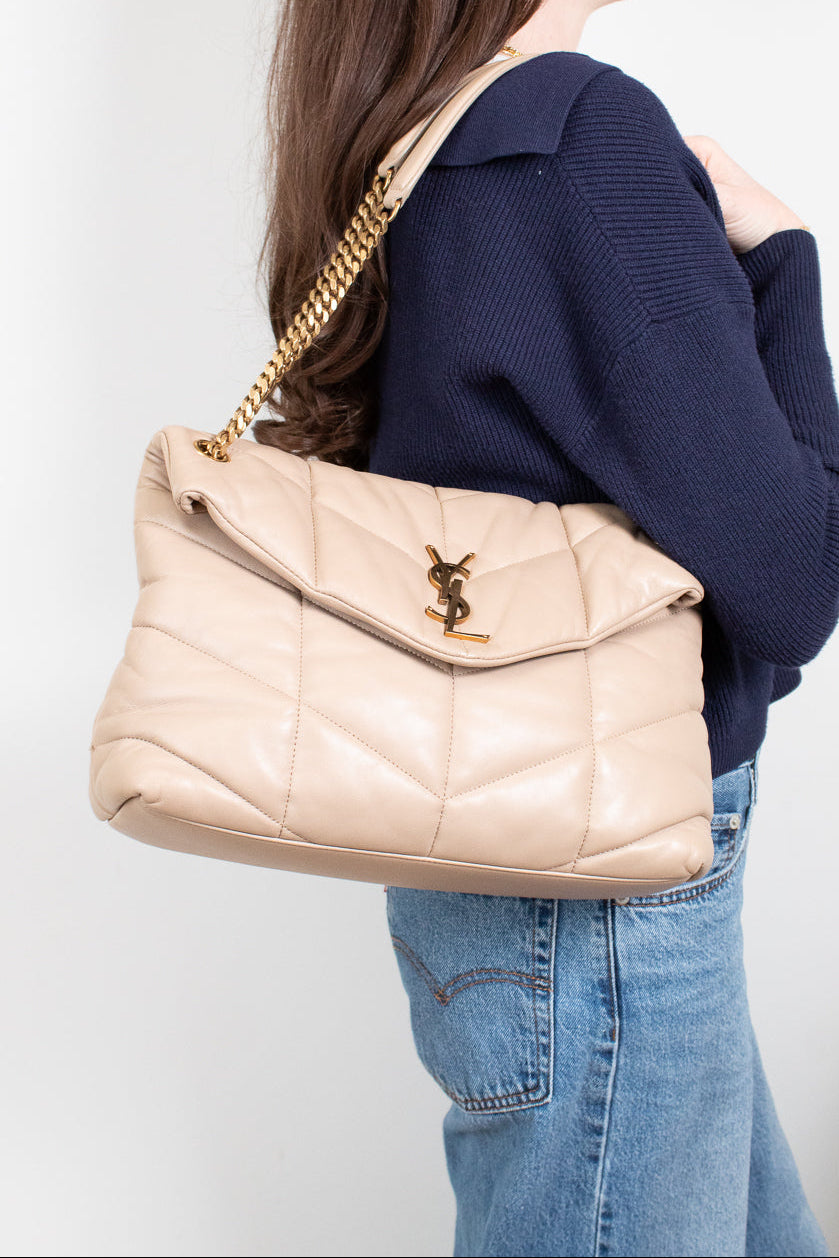 Person wearing a navy sweater and blue jeans with a beige quilted handbag featuring a gold chain strap.