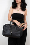 Woman holding a black handbag against a plain background