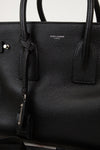 Black leather handbag with 'Saint Laurent' branding on a light gray background