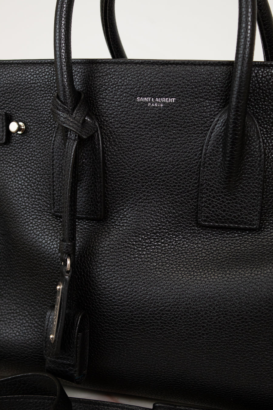 Black leather handbag with 'Saint Laurent' branding on a light gray background