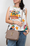 Person wearing a colorful sleeveless top with graphics and holding a beige handbag.