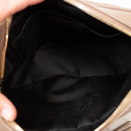 Close-up of a beige handbag with a tassel detail, held open to show the black interior.