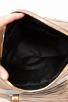 Close-up of a beige handbag with a tassel detail, held open to show the black interior.
