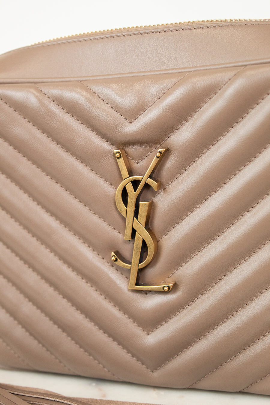 Beige quilted handbag with gold logo on a white background