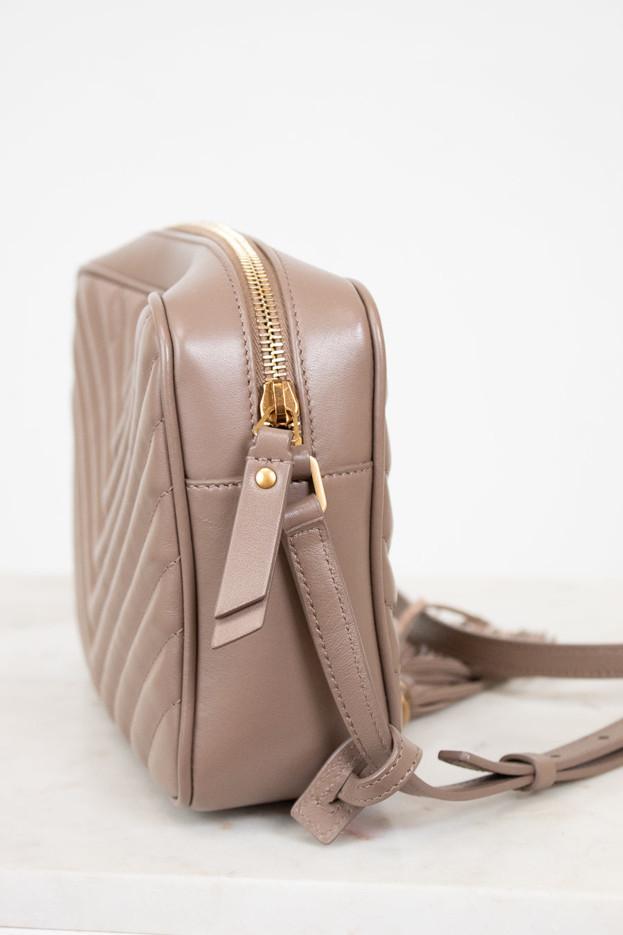 Beige quilted handbag with gold zipper on a light gray background