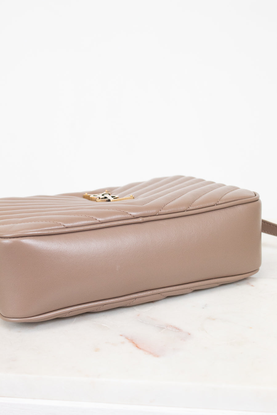 Taupe handbag with a gold clasp on a light pink background