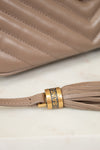 Close-up of a beige handbag with a tassel detail and 'Saint Laurent' branding.