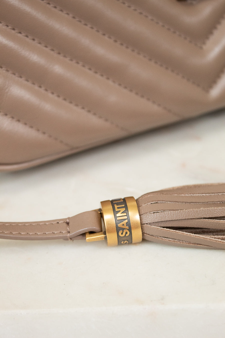 Close-up of a beige handbag with a tassel detail and 'Saint Laurent' branding.