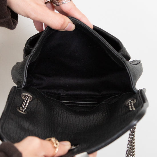Person opening a black handbag with a chain strap on a light gray background