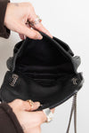 Person opening a black handbag with a chain strap on a light gray background