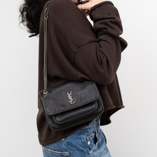 Person wearing a black textured handbag with a brand logo on a white background