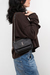 Person wearing a black textured handbag with a brand logo on a white background