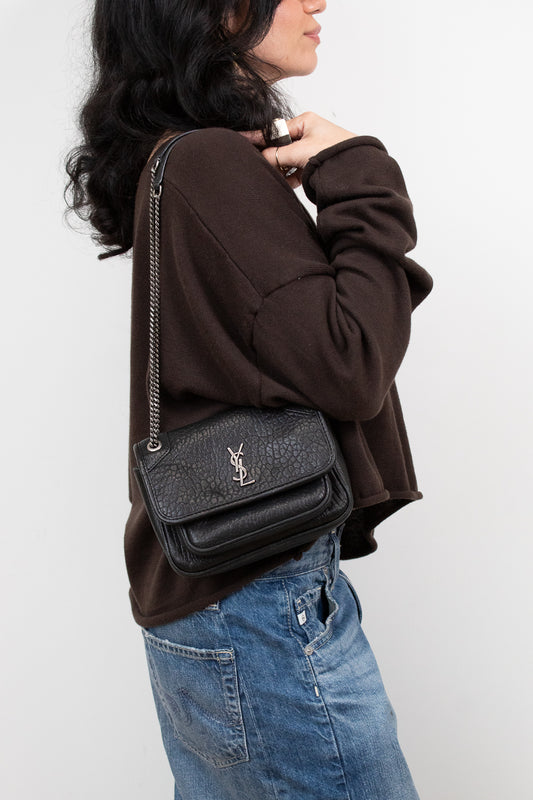 Person wearing a black textured handbag with a brand logo on a white background