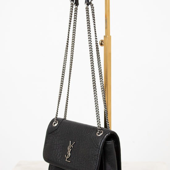 Black handbag with chain strap on a wooden stand against a white background