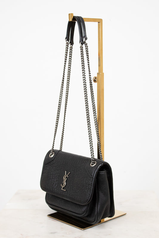 Black handbag with chain strap on a wooden stand against a white background