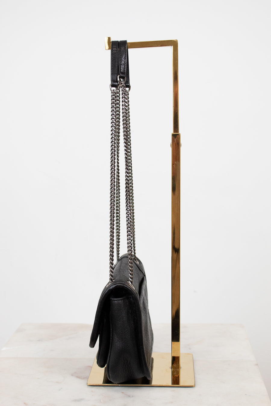 Black handbag with a chain detail on a gold stand against a white background