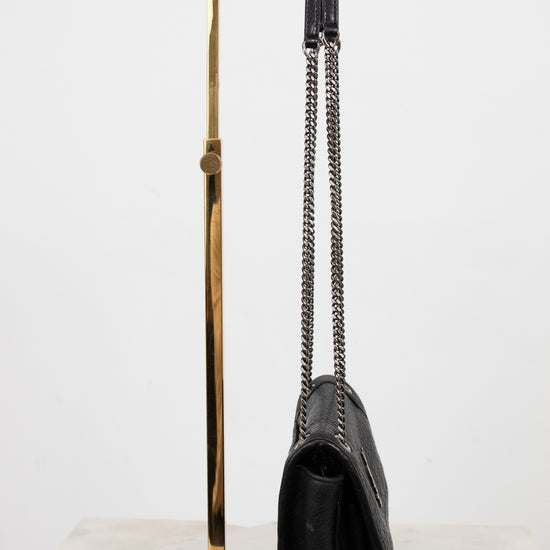 Black handbag on a gold stand against a white background