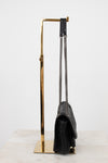 Black handbag on a gold stand against a white background