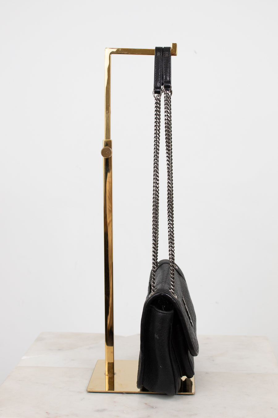 Black handbag on a gold stand against a white background