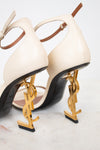 Beige high-heeled shoes with gold YSL logo on a white background