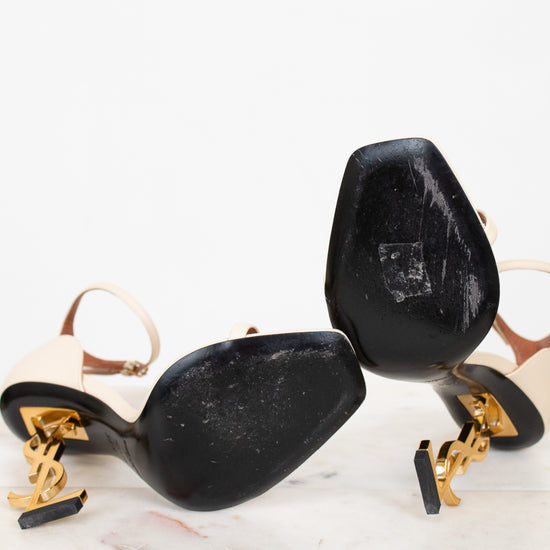 White high-heeled shoes with gold accents and black soles on a white background
