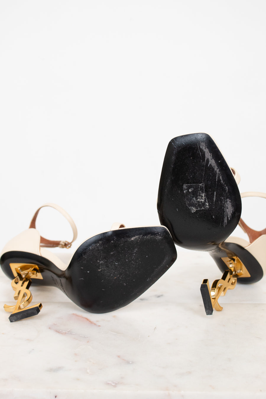 White high-heeled shoes with gold accents and black soles on a white background