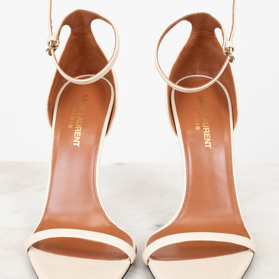 Pair of white high-heeled shoes with brown interior soles on a light background