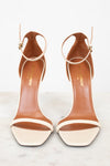 Pair of white high-heeled shoes with brown interior soles on a light background
