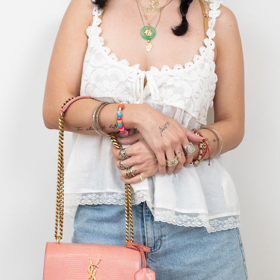 Pink lizard bag with gold logo and chain details being held by person