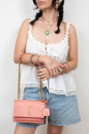 Pink lizard bag with gold logo and chain details being held by person