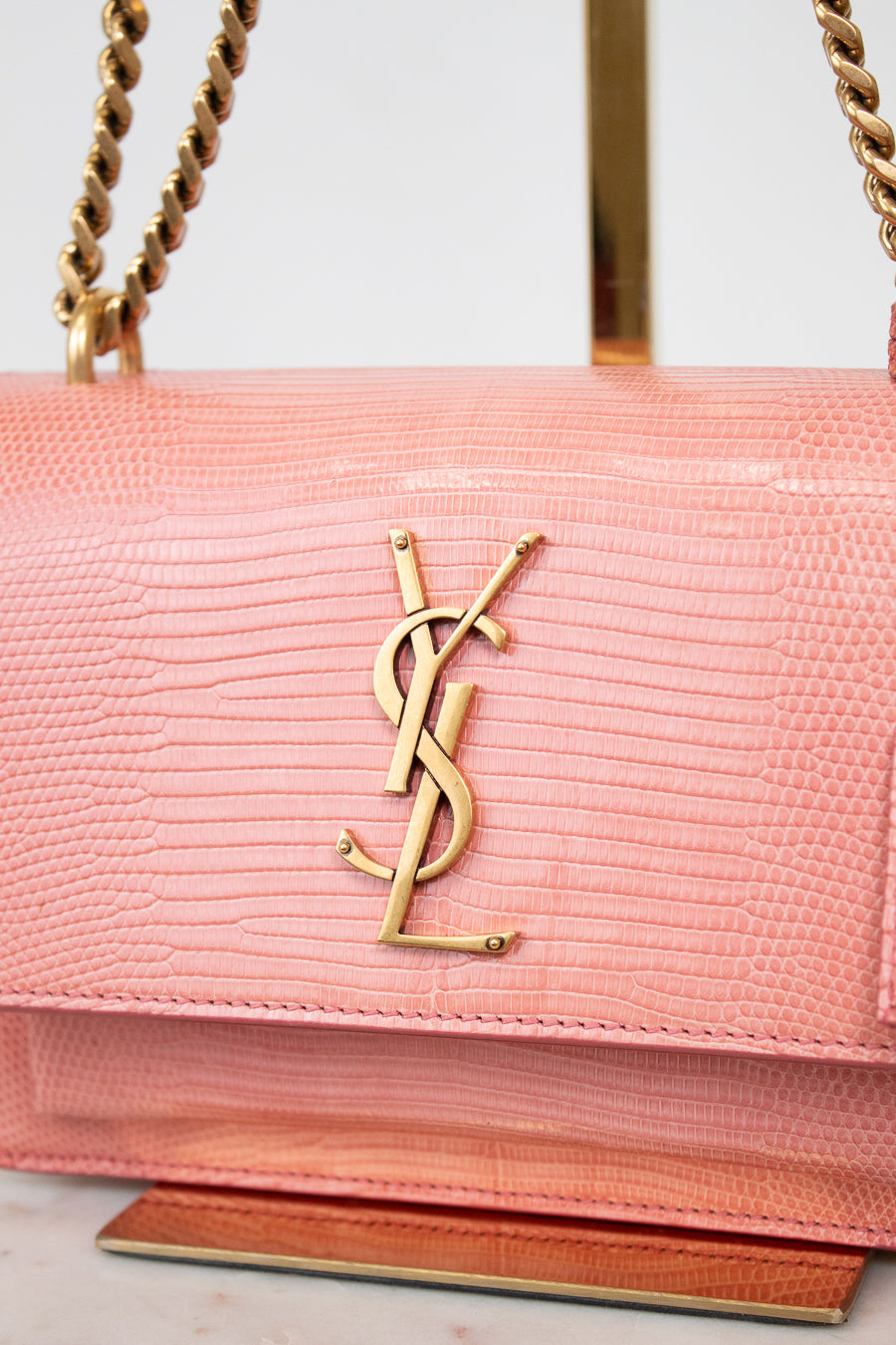 Close-up of gold 'YSL' logo against pink lizard leather