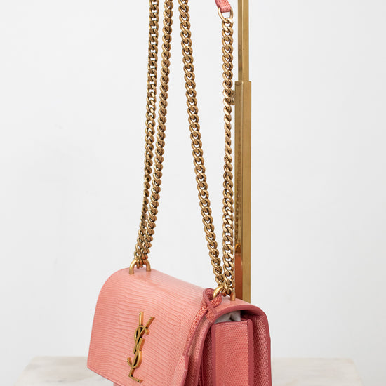 Pink lizard bag with visible 'YSL' logo with gold chain straps on gold stand