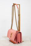 Pink lizard bag with visible 'YSL' logo with gold chain straps on gold stand