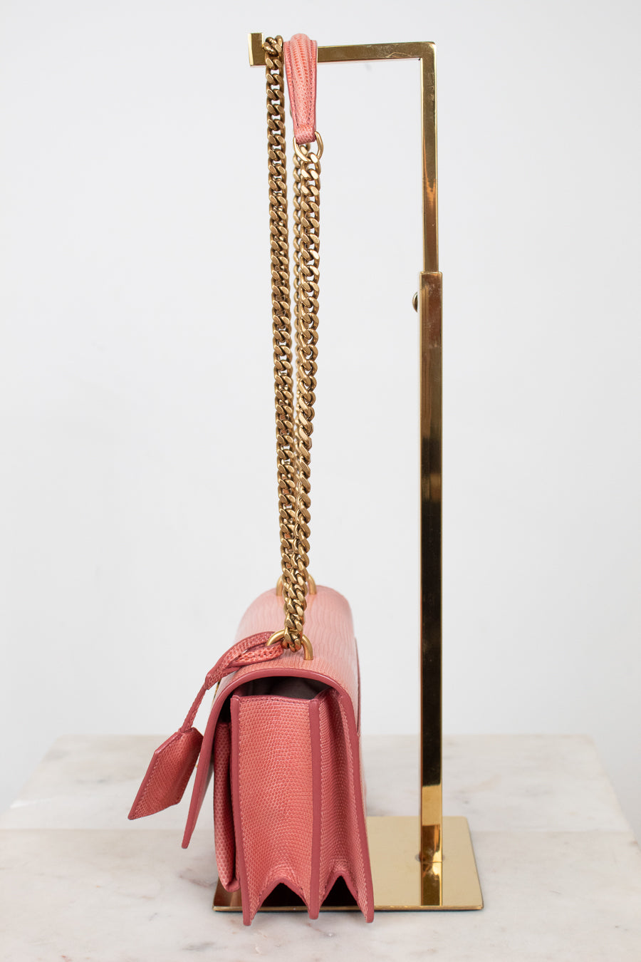 Side view of pink lizard bag with gold chain straps on gold stand