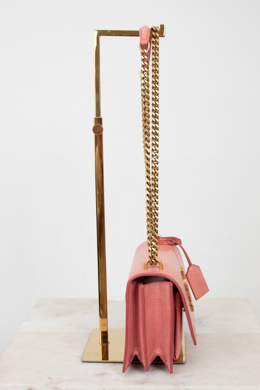 Side view of pink lizard bag with gold chain straps on gold stand
