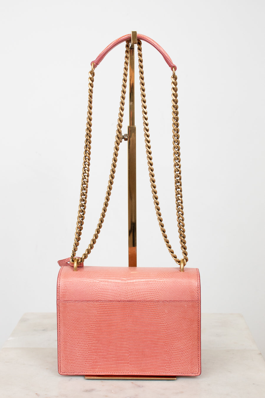 Back view of pink lizard bag with gold chain straps on gold stand 