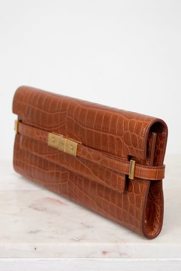 Brown crocodile-patterned clutch bag with gold clasp on a marble surface