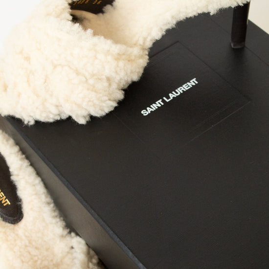 Saint Laurent fluffy cream shearling slide heel resting on a black branded shoebox against a clean white background.